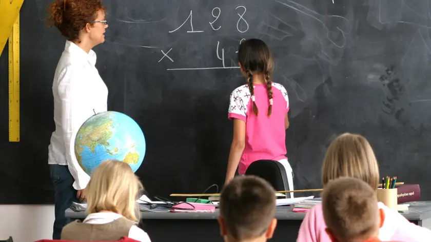 intÃ©rieur salle de classe, institutrice regardant fillette de dos au tableau, faisant multiplication, garÃ§ons et fillettes assis au 1er plan