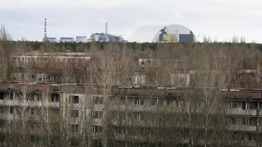 This photo taken Wednesday, March 23, 2016 shows abandoned apartment buildings in the town of Pripyat near Chernobyl, Ukraine, with a chimney, left, at the destroyed reactor and a gigantic arch-shape confinement to cover the remnants of the exploded reactor, in the back, at the Chernobyl nuclear power plant. Thirty years after the worlds worst nuclear accident, the Chernobyl nuclear power plant is surrounded by both a hushed desolation and clangorous activity, the sense of a ruined past and a difficult future. (ANSA/AP Photo/Efrem Lukatsky)