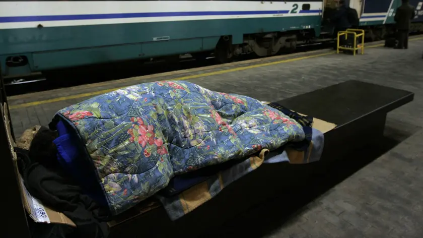 Un clochard dorme sotto le coperte per strada in una foto d'archivio. ANSA / MASSIMO PERCOSSI