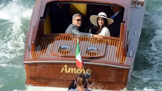 George Clooney, flanked by his wife Amal Alamuddin, sit on a water-taxi after leaving the city hall in Venice, Italy, Monday, Sept. 29, 2014. George Clooney married human rights lawyer Amal Alamuddin Saturday, the actor's representative said, out of sight of pursuing paparazzi and adoring crowds. (AP Photo/Luigi Costantini)