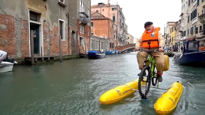 Patrizio Roversi mentre pedala su una bici galleggiante in città