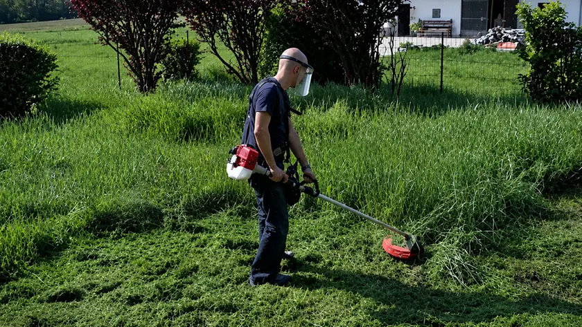 Un uomo al lavoro con il decespugliatore in giardino