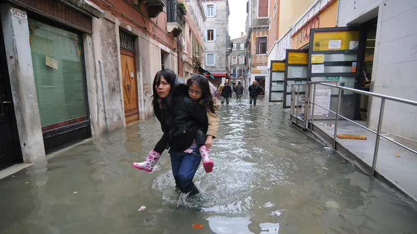 20081201 - VENEZIA - WEA - MALTEMPO: RECORD ACQUA ALTA A VENEZIA,INCIDENTI AL NORD: Una giovane con in braccio una bambina cerca di camminare lungo una delle calli del centro storico di Venezia ricoperta dall'acqua alta. Da oltre vent'anni non si registrava un livello simile di acqua alta nella città veneta. Una citta' paralizzata, oggi Venezia, dove ai problemi dell'acqua alta su misure eccezionali (160 centimetri previsti a mezzogiorno), si aggiunge lo sciopero dei trasporti pubblici, proclamato dalla sigla Rdb Cub. Sulla laguna di Venezia, intanto, insiste un vento di scirocco che impedisce il deflusso delle acque. ANSA/ANDREA MEROLA/I51.