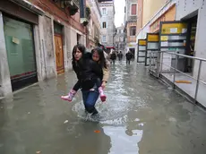 20081201 - VENEZIA - WEA - MALTEMPO: RECORD ACQUA ALTA A VENEZIA,INCIDENTI AL NORD: Una giovane con in braccio una bambina cerca di camminare lungo una delle calli del centro storico di Venezia ricoperta dall'acqua alta. Da oltre vent'anni non si registrava un livello simile di acqua alta nella città veneta. Una citta' paralizzata, oggi Venezia, dove ai problemi dell'acqua alta su misure eccezionali (160 centimetri previsti a mezzogiorno), si aggiunge lo sciopero dei trasporti pubblici, proclamato dalla sigla Rdb Cub. Sulla laguna di Venezia, intanto, insiste un vento di scirocco che impedisce il deflusso delle acque. ANSA/ANDREA MEROLA/I51.