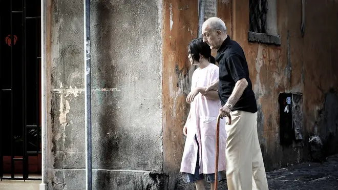 Una badante straniera accompagna un anziano signore per le vie del centro di Roma,in una foto del 2 settembre 2009. . I costi dell'assistenza ai disabili pesano sempre di piu' sulle loro famiglie. E in tempo di crisi i parenti studiano strategie di ''arrangiamento organizzato'' che passano anche attraverso il volontariato, prima di rivolgersi al settore privato o alle badanti. E' quanto emerge dal 44mo.Rapporto annuale del Censis sulla situazione sociale del Paese, che ha stimato in oltre 56mila euro, il costo di un malato di Alzheimer all'anno. Cifra che scende a 11.250 euro/anno per un paziente con artrite reumatoide e circa 15mila euro per i malati di insufficienza renale cronica in dialisi. ANSA/ GUIDO MONTANI