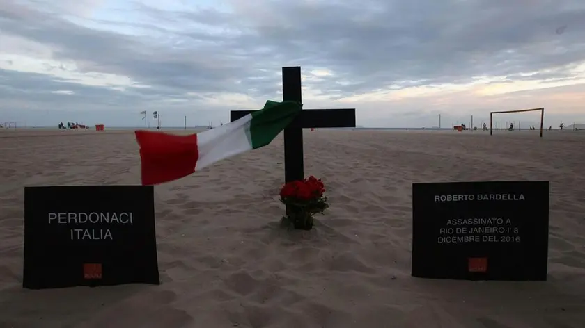 epa05668306 An Italian flag tied to a cross in honor of the Italian tourist Roberto Bardella who was fatally shot on 08 December, at Copacabana Beach in Rio de Janeiro, Brazil, 09 December 2016. Roberto Bardella was fatally shot in the 'Morro dos Prazeres' favela on 08 December. His compatriot with whom he was traveling, Rino Polato, was found unharmed at the entrance to the favela. The sign (L) reads, in Italian, 'Forgive us, Italy'. EPA/MARCELO SAYAO