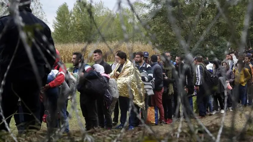 FILE - In this Saturday, Sept. 26, 2015 file photo, a group of migrants, seen through razor wire, crosses a border from Croatia near the village of Zakany, Hungary. Together, Hungary and the Czech Republic took in just around 1,000 asylum-seekers last year. Still, rallying cries against migration have dominated the debates ahead of upcoming ballots in the two Central European countries. Hungary is holding a government-sponsored referendum on Oct. 2 2016, seeking political support for the rejection of any future mandatory EU quotas to accept refugees. (ANSA/AP Photo/Petr David Josek, file) [CopyrightNotice: Copyright 2016 The Associated Press. All rights reserved.]