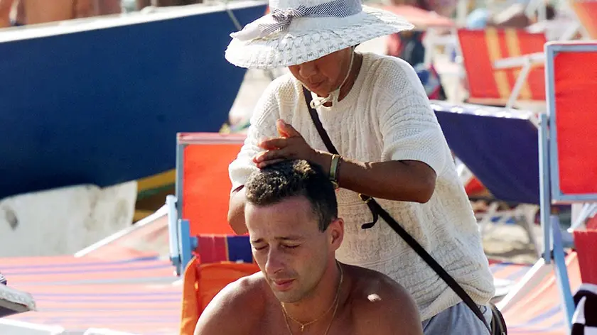 20010813- BOLOGNA- FERRAGOSTO : ESODO DALLE CITTA' - Un bagnate alle prese con una massaggiatrice cinese Nella spiaggia di Riccione (Rimini)durante le festivita' di Ferragosto. Le ottime previsioni meteorologiche hanno favorito l'esodo dalle citta' per le localita' di vacanza. GIORGIO BENVENUTI/ANSA /ji