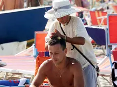 20010813- BOLOGNA- FERRAGOSTO : ESODO DALLE CITTA' - Un bagnate alle prese con una massaggiatrice cinese Nella spiaggia di Riccione (Rimini)durante le festivita' di Ferragosto. Le ottime previsioni meteorologiche hanno favorito l'esodo dalle citta' per le localita' di vacanza. GIORGIO BENVENUTI/ANSA /ji