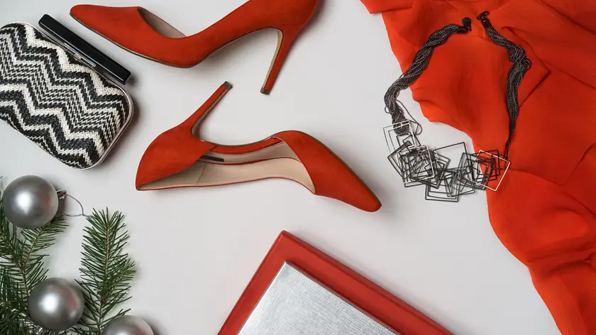 Top view to New Year and Christmas party outfit composition red shoes accessories jewelry makeup clutch hourglass fir tree with balls white background. Party date night conception. Flat lay, copy space