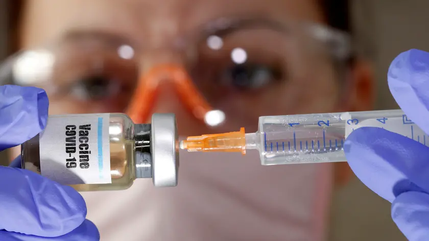 FILE PHOTO: A woman holds a small bottle labeled with a "Vaccine COVID-19" sticker and a medical syringe in this illustration taken April 10, 2020. REUTERS/Dado Ruvic/Illustration/File Photo