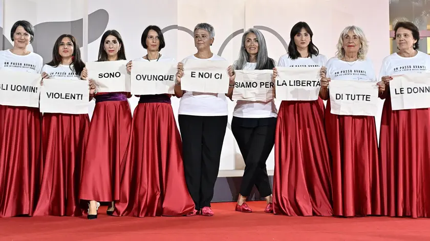 Alcune delle molte partecipanti all’iniziativa contro la violenza verso le donne mostrano il loro messaggio sul red carpet della Mostra del Cinema