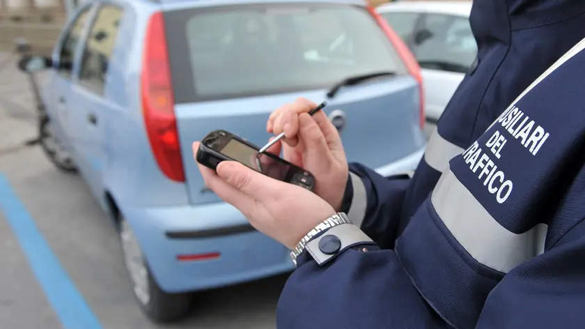 Un'ausiliaria del traffico controlla una vettura parcheggiata entro strisce blu a Pontedera, in un'immagine d'archivio. ANSA/FRANCO SILVI