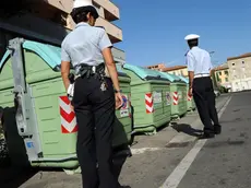 Alcuni agenti della polizia municipale controllano i cassonetti all' entrata del comune di Lucca. Basta rifiuti gettati nei cassonetti.dagli abitanti degli altri Comuni limitrofi. Cosi', per impedire lo smaltimento abusivo, il Comune di Lucca ha deciso di mettere.i vigili urbani, anche in borghese, e le guardie zoofile a presidiare i cassonetti. E' ormai guerra dell'immondizia tra Lucca e i Comuni ai suoi confini est, sud-est e nord. L'allarme, con conseguente giro di vite, e' scattato quando l'amministrazione lucchese e la societa' Sistema Ambiente si sono accorte che nel 2010 la spazzatura conferita nei cassonetti era aumentata di 1300 tonnellate..ANSA/FRANCO SILVI